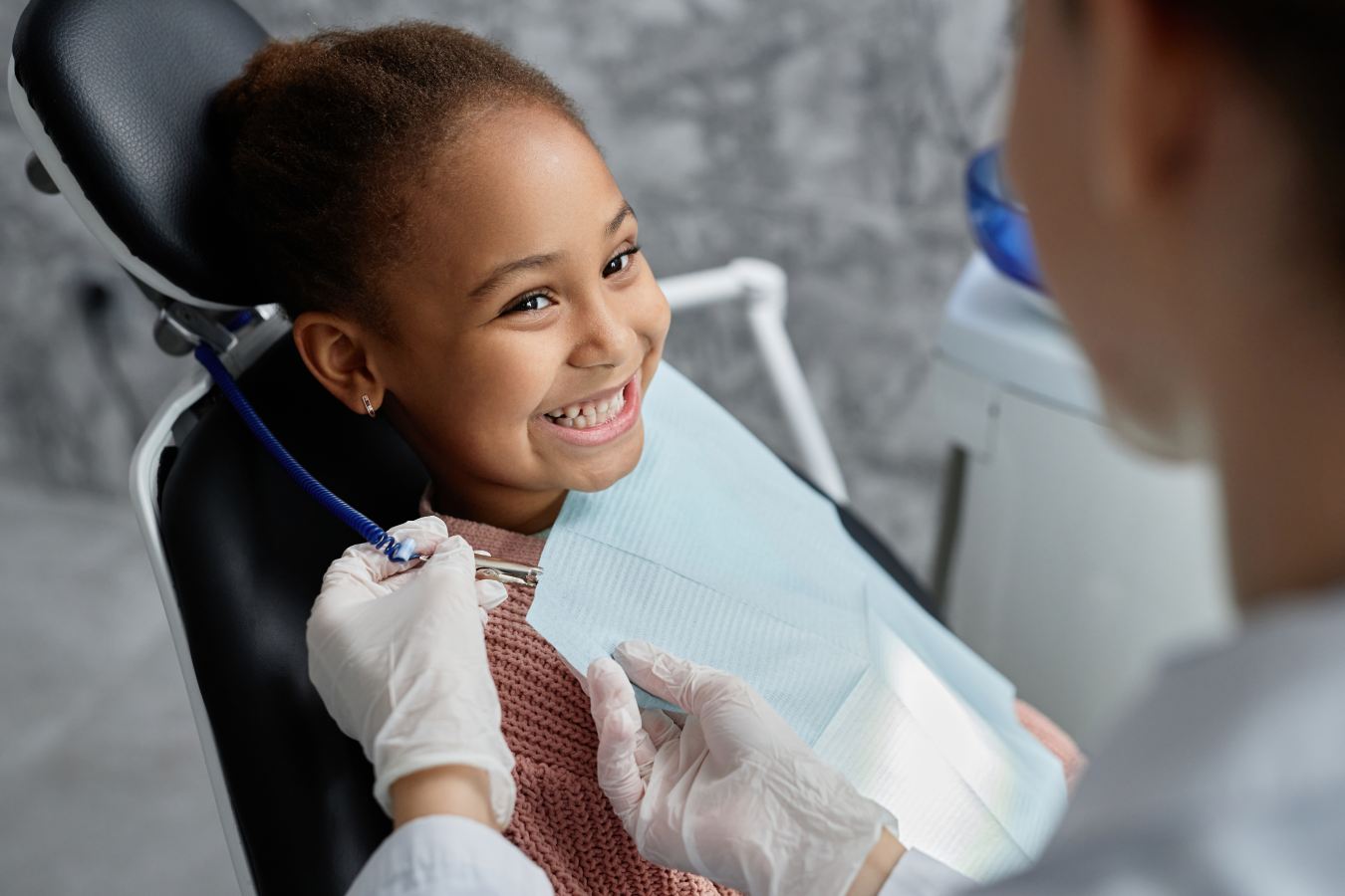 Young child smiling at orthodontist as they place a napkin around her neck
